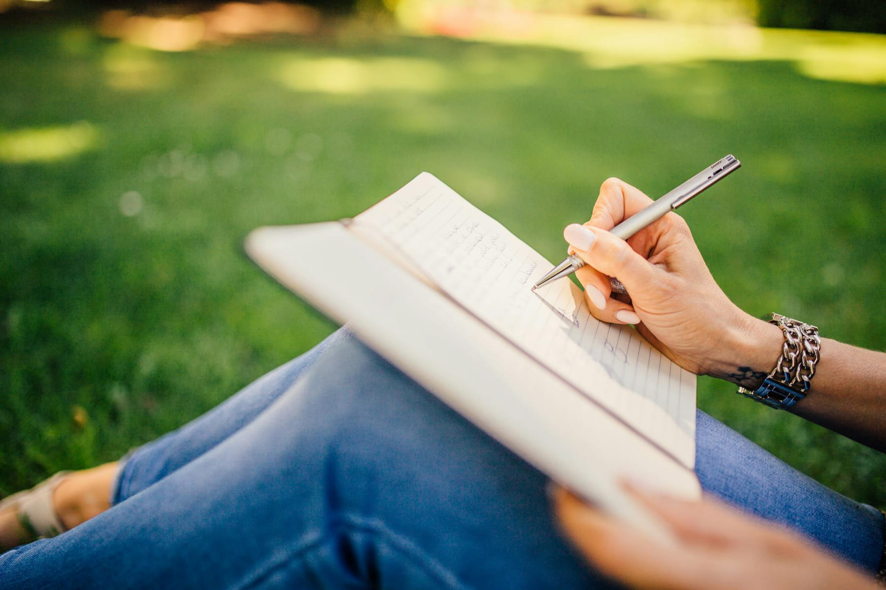 Person writes in a notebook on a sunny day. Focus on hands and pen outdoors. on Inner Progress Project