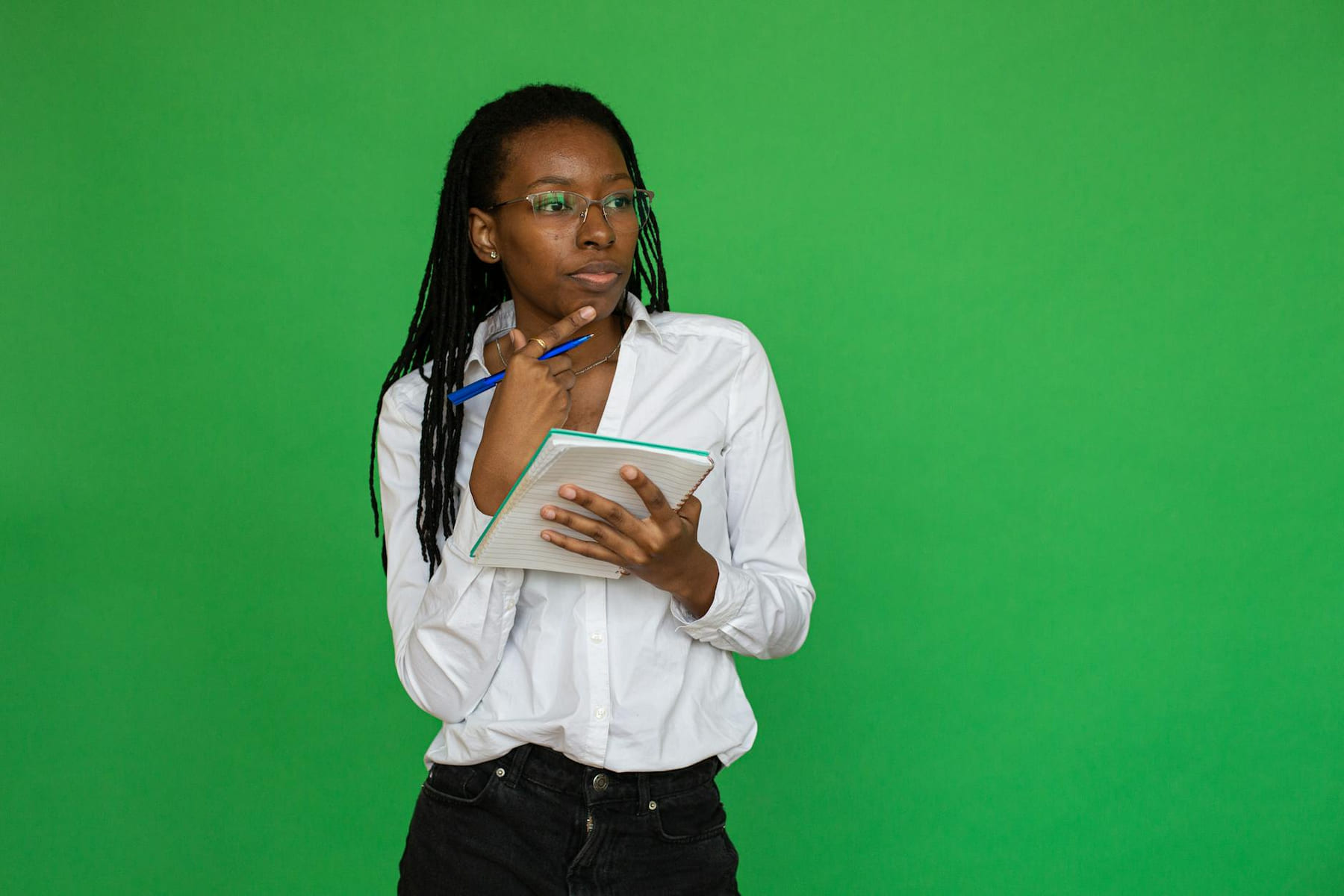 Pensive woman holding a notebook and pen, contemplating on a vibrant green backdrop. on Inner Progress Project