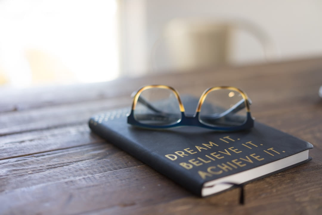 black and brown eyeglasses on book on brown wooden table on Inner Progress Project